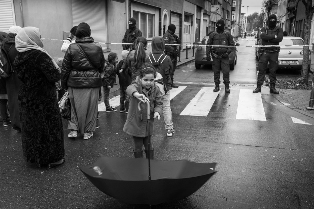 A girl plays with her umbrella in front of masked policemen in the Ransfort street who prevent access to the security perimeter set up during an operation around the Delaunoy street in the predominantly Muslim borough of Molenbeek Saint Jean, in connection with the terrorists attacks in Paris.