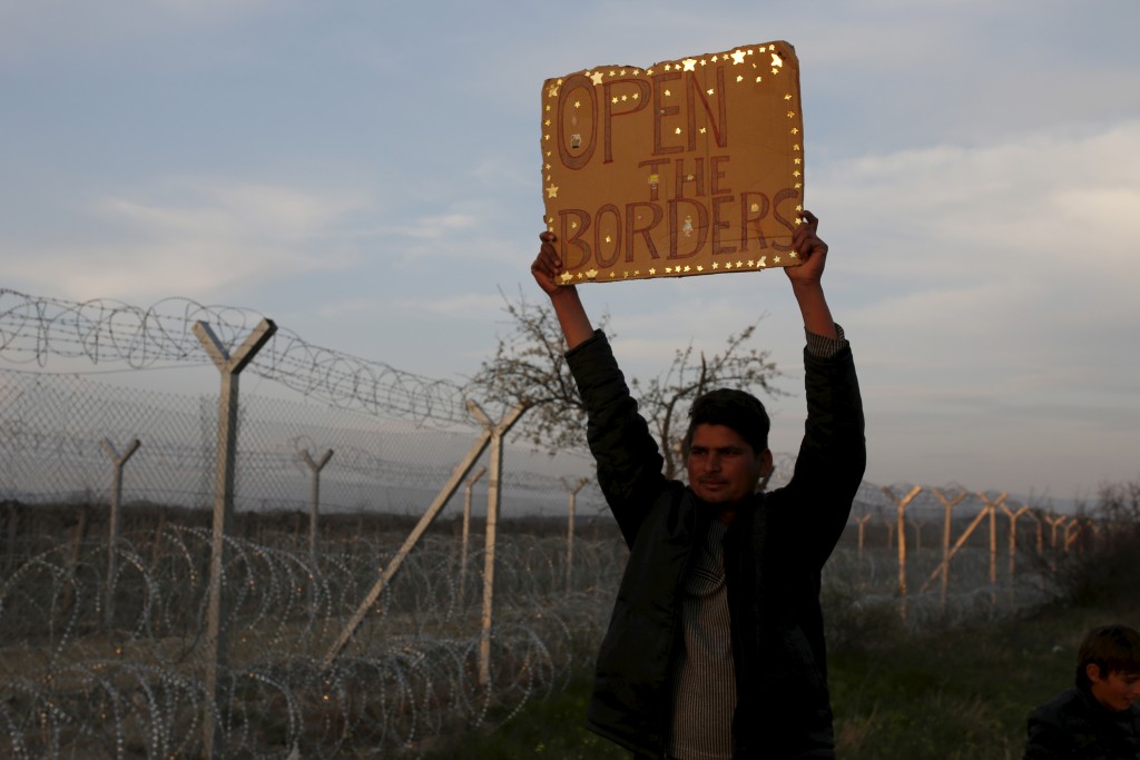 A migrant holds a sign in front of the Greek-Macedonian border fence near the village of Idomeni, Greece, March 28, 2016. Credit: REUTERS/Marko Djurica