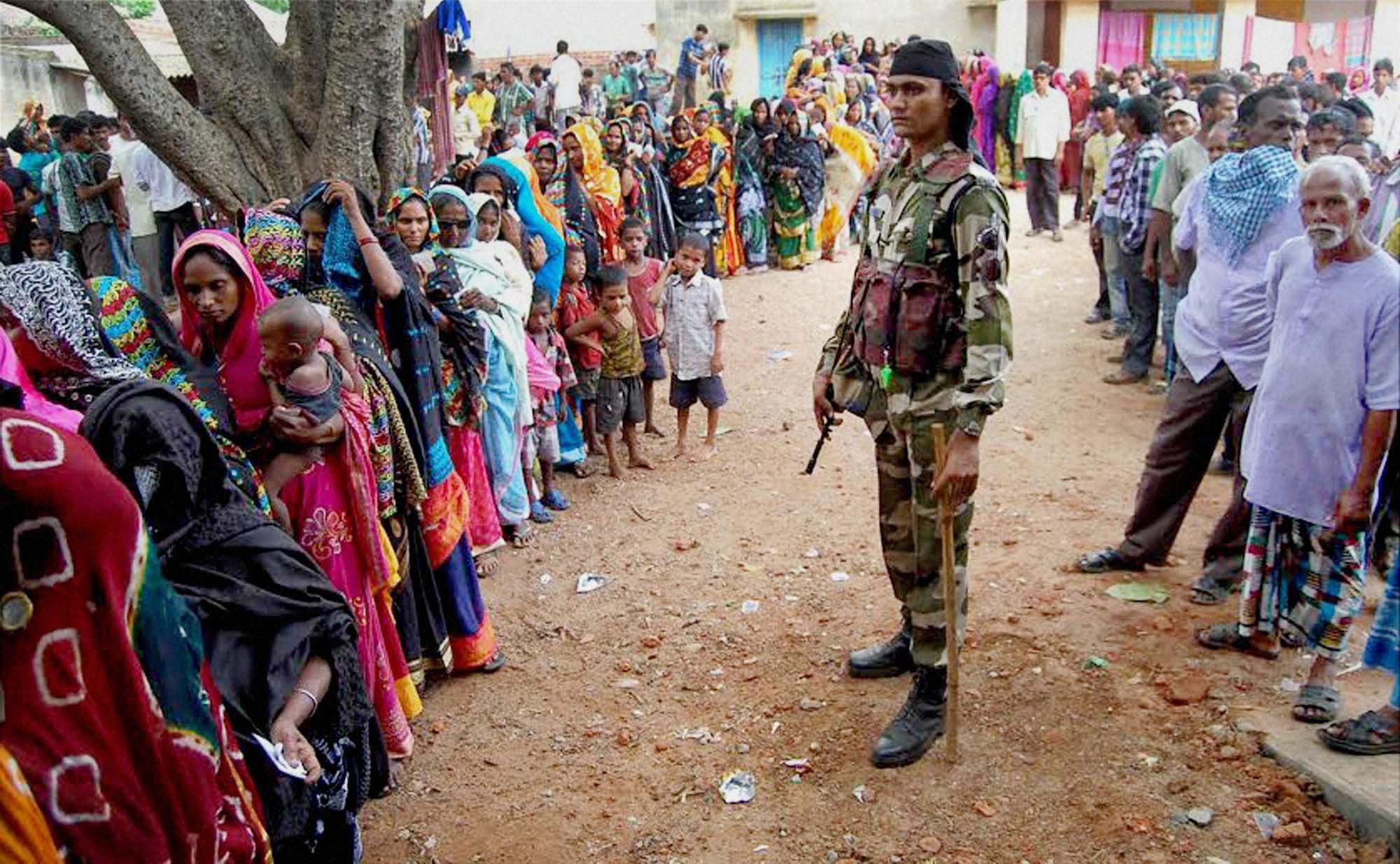 Bankura: Central Force Jawan keeps vigil while voters stand in a queue to cast vote at a polling station during the 2nd part of 1st phase West Bengal assembly elections in Bankura on Monday. Credit: PTI