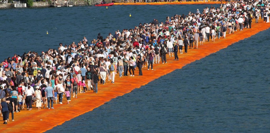 People walk the 'The Floating Piers' by Bulgarian artists Christo and Jeanne-Claude on Lake Iseo during the opening of the art work near Sulzano, northern Italy, June 18, 2016. The 'Floating Piers' with their bright orange covers will be open until July 03 and will connect the two towns Sulzano and Monte Isola. Credit: EPA/Filippo Venezia