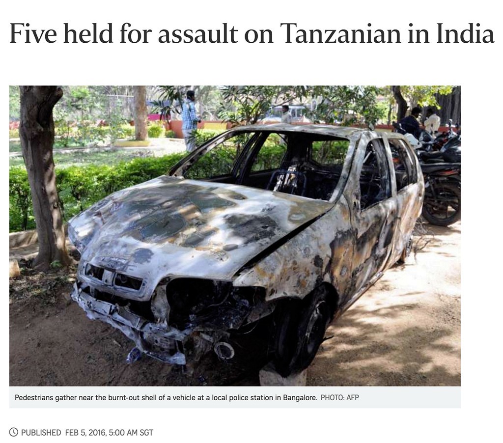 Pedestrians gather near the burnt-out shell of a vehicle at a local police station in Bangalore. Credit: AFP