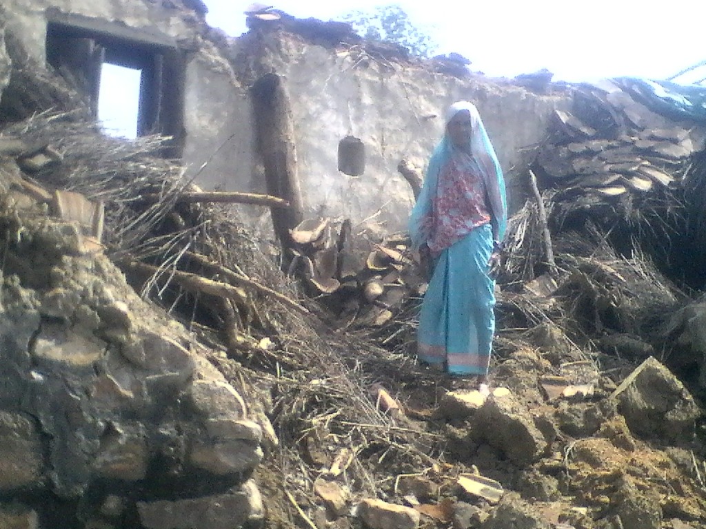 A woman stands in front of her collapsed house. Credit: Special Arrangement