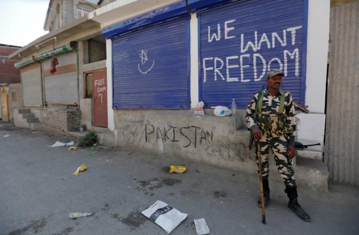 An Indian policeman stands guard near shops painted with graffiti during curfew in Srinagar, August 5, 2016. Credit: Reuters/Danish Ismail