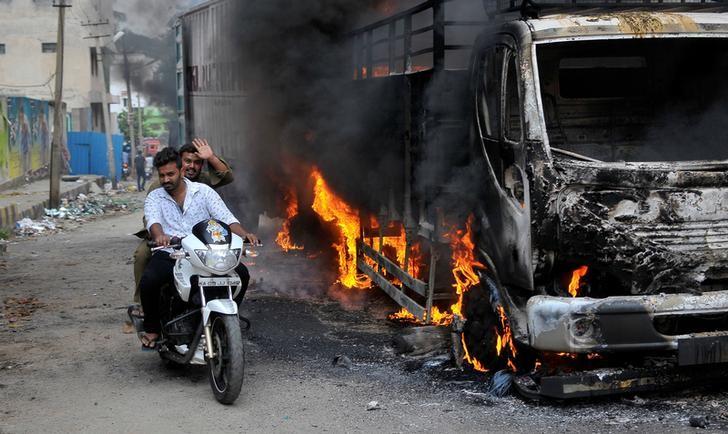 Men ride a motorcycle past a lorry in Bengaluru, which was set on fire by protesters after the Supreme Court ordered Karnataka to release 12,000 cubic feet of water per second every day from the Cauvery river. Credit: Reuters