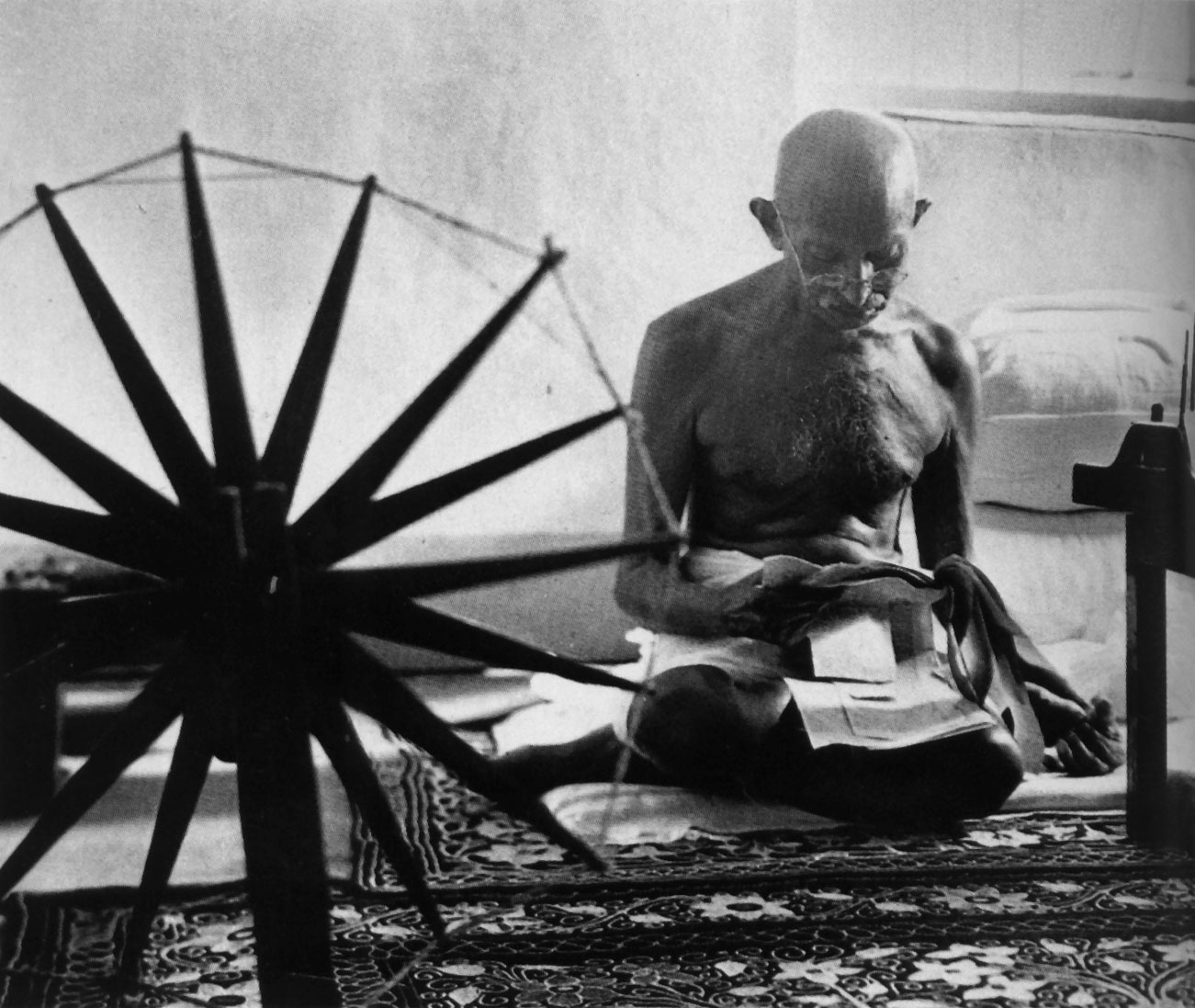 Gandhi reading next to his spinning wheel. Credit: eBay