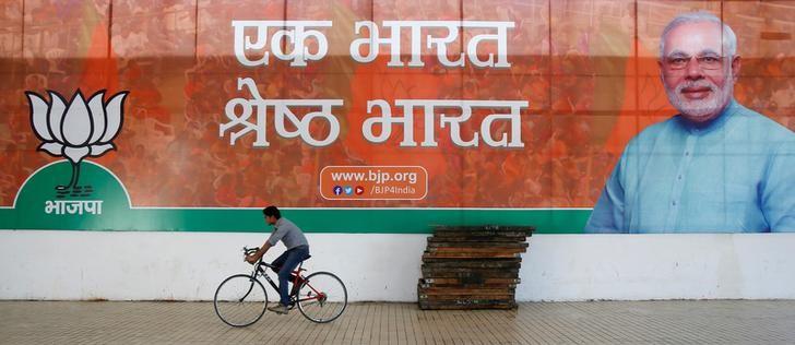 A worker of the Bharatiya Janata Party (BJP) rides his bicycle past the party's campaign billboard featuring Prime Minister Narendra Modi outside their party headquarters in New Delhi, India, February 10, 2015. Credit: Reuters/Anindito Mukherjee/File Photo