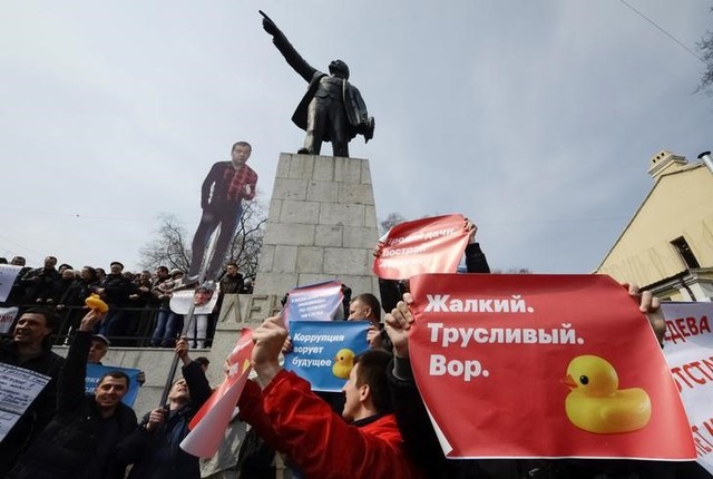 Opposition supporters hold posters and a cutout figure depicting Prime Minister Dmitry Medvedev during a rally in front of a monument of Soviet state founder Vladimir Lenin in Vladivostok, Russia, March 26, 2017. Sign on right poster reads:
