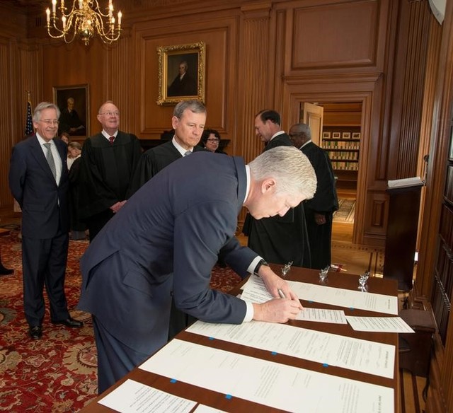 Chief justice of the US John Roberts (C) looks on as judge Neil Gorsuch (R) signs the constitutional oath during swearing-in ceremony at the Supreme Court in Washington, US, April 10, 2017. Credit: Reuters/Supreme Court of the US