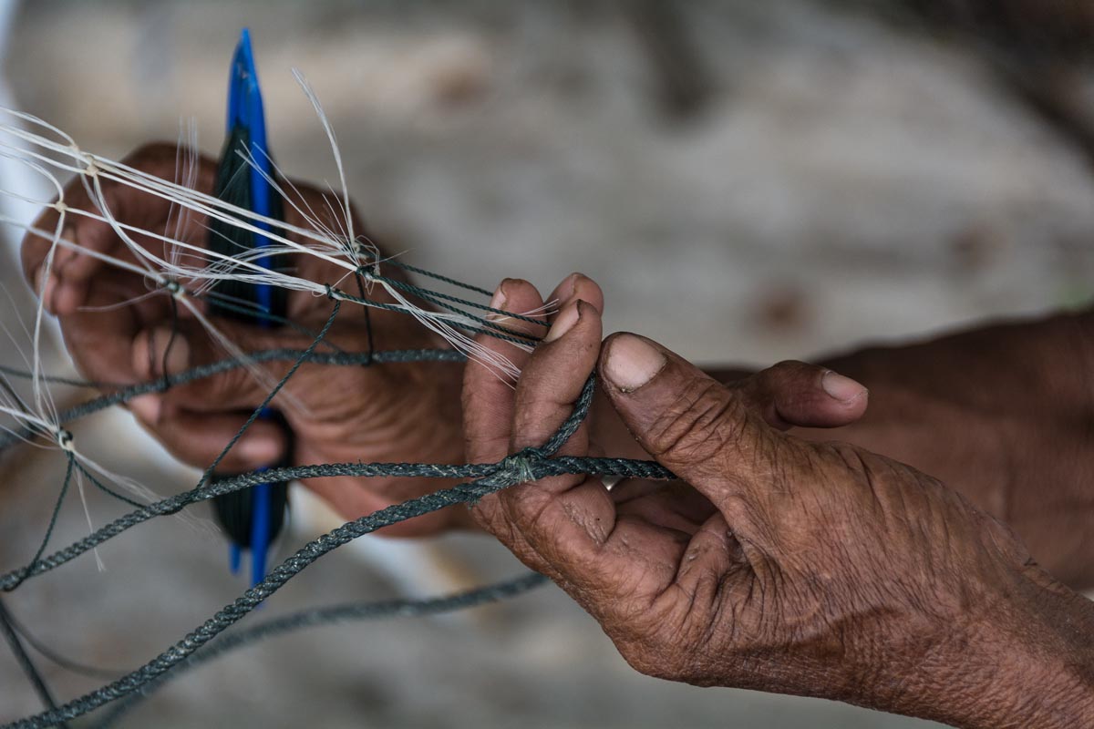 Mr Kamaruddin, 70, is fixing his net on the beach next to his home at Tanjung Tokong, Penang Island. Credit: Rod Harbinson via Mongabay