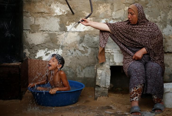 A Palestinian woman bathes her son with water from a tank, filled by a charity, inside their dwelling in Khan Younis, in the southern Gaza Strip, July 3, 2017. Credit: Reuters/Mohammed Salem/Files