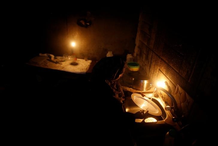 A Palestinian woman washes dishes in her kitchen as she uses a candle light during a power cut in Beit Lahiya town, in the northern Gaza Strip, July 13, 2017. Credit: Reuters/Mohammed Salem/Files