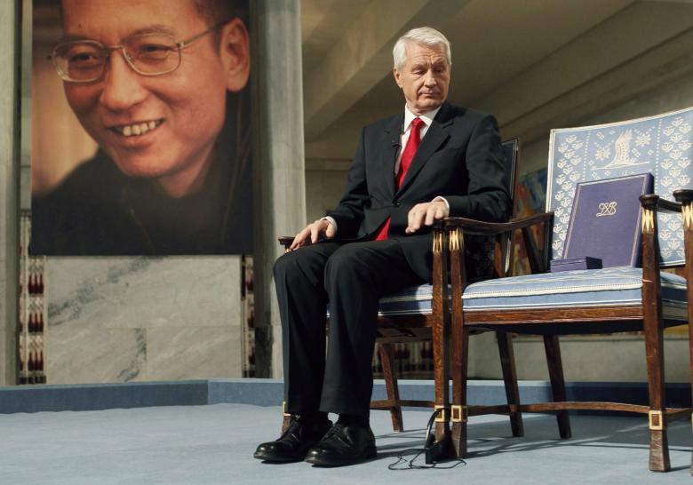 Chairman of the Norwegian Nobel Committee Thorbjoern Jagland looks down at the Nobel certificate and medal on the empty chair where Nobel Peace Prize winner Liu Xiaobo would have sat, as a portrait of Liu is seen in the background, during the ceremony at Oslo City Hall December 10, 2010. Credit: Reuters/Heiko Junge/Scanpix Norway/Pool