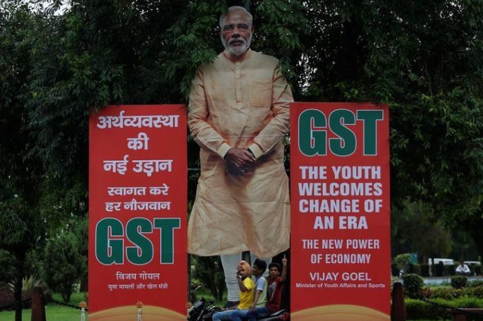 A boy riding a motorcycle gestures as he passes a hoarding in favour of the implementation of the Goods and Services Tax (GST) at a street in New Delhi, June 30, 2017. Credit: Reuters/Adnan Abidi/Files