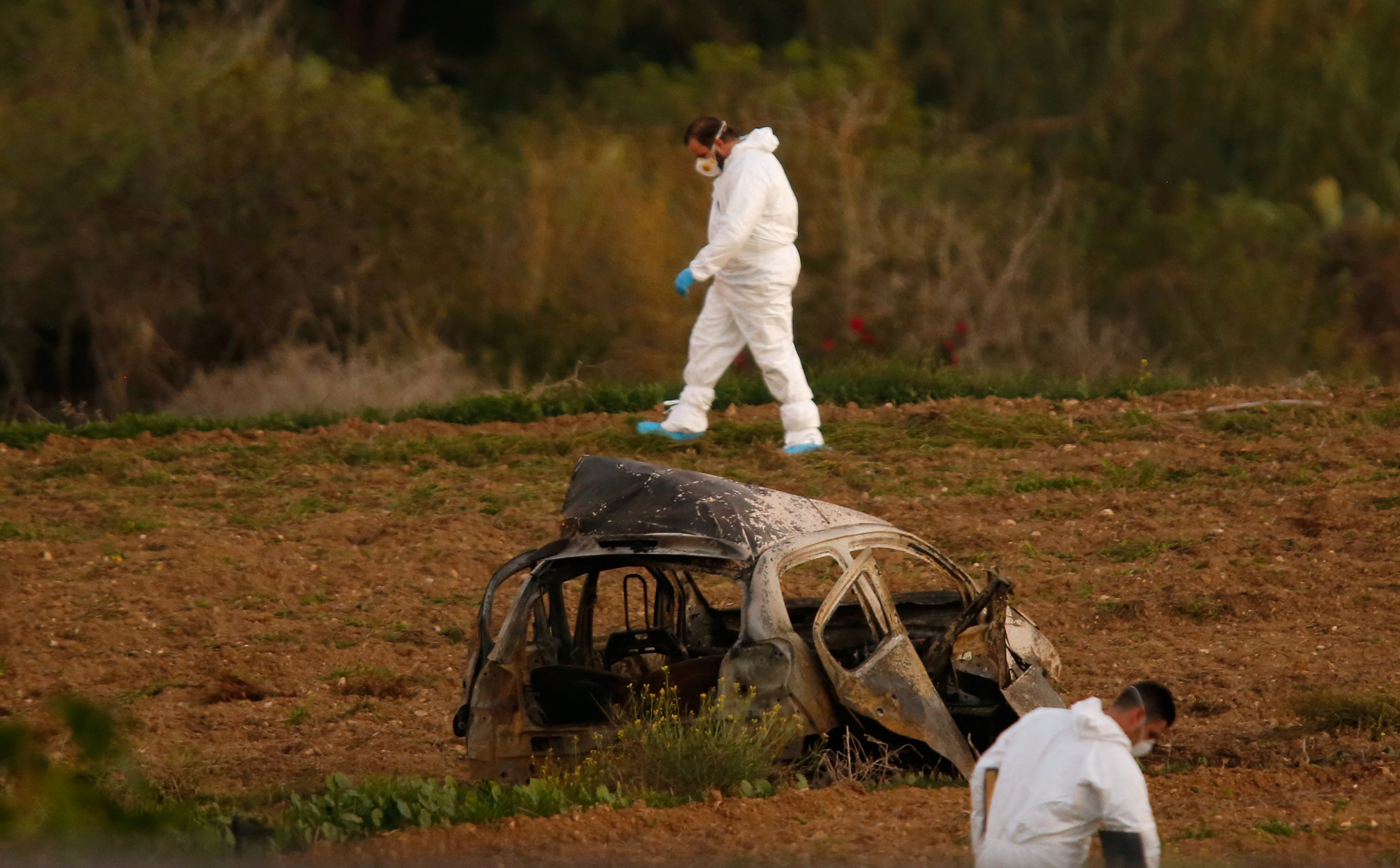 Forensic experts walk in a field after a powerful bomb blew up a car (Foreground) and killed investigative journalist Daphne Caruana Galizia in Bidnija, Malta, October 16, 2017. Credit: Reuters/Darrin Zammit Lupi
