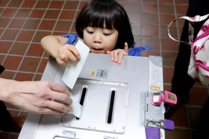 A girl casts her father's ballot for a national election at a polling station in Tokyo, Japan October 22, 2017. Credit: Reuters/Kim Kyung-Hoon