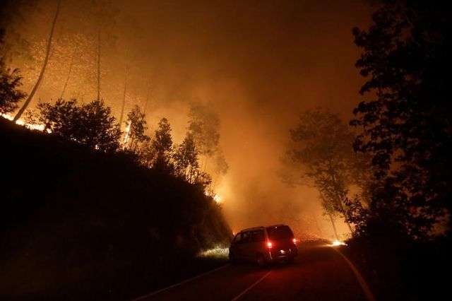 A vehicle turns around as a forest fire burns by the road near Vigo, Spain, October 15, 2017. Credit: Reuters