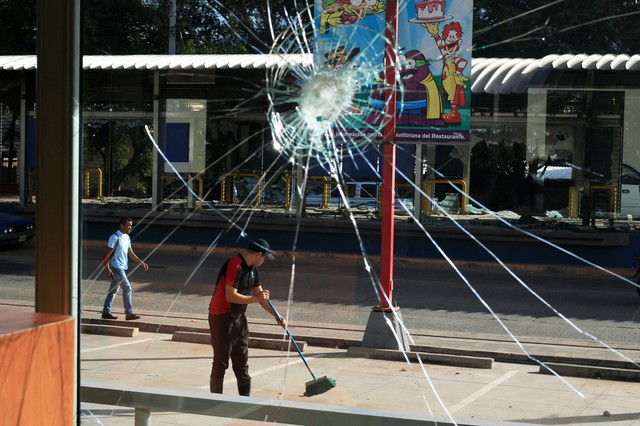 A broken restaurant window is seen after being looted while an employee sweeps the pavement, caused by the delayed vote count of he presidential election in Tegucigalpa, Honduras December 2, 2017. Credit: Reuters/Jorge Cabrera