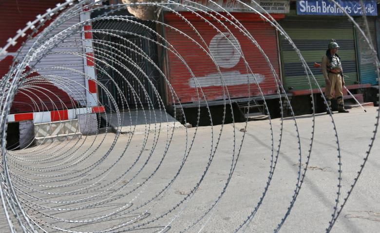 An policeman stands guard next to concertina wire laid across a road during a curfew in downtown Srinagar. Credit: Reuters/Danish Ismail