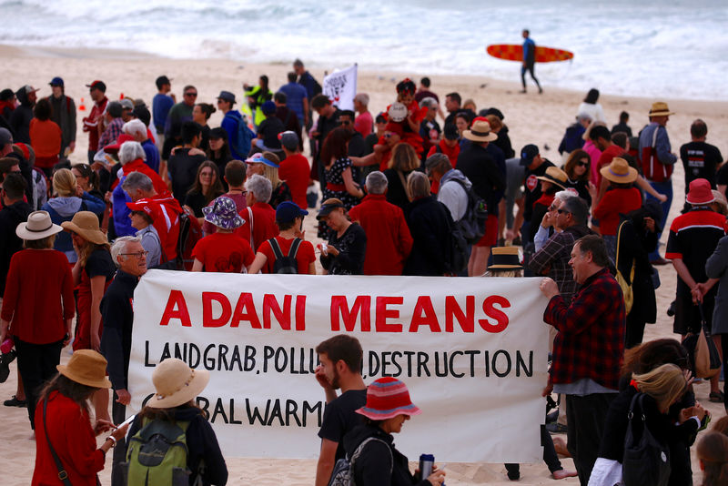A surfer carries his board as he walks behind protesters participating in a national Day of Action against the Indian mining company Adani's planned coal mine project in north-east Australia, at Sydney's Bondi Beach in Australia, October 7, 2017. Credit: Reuters/David Gray