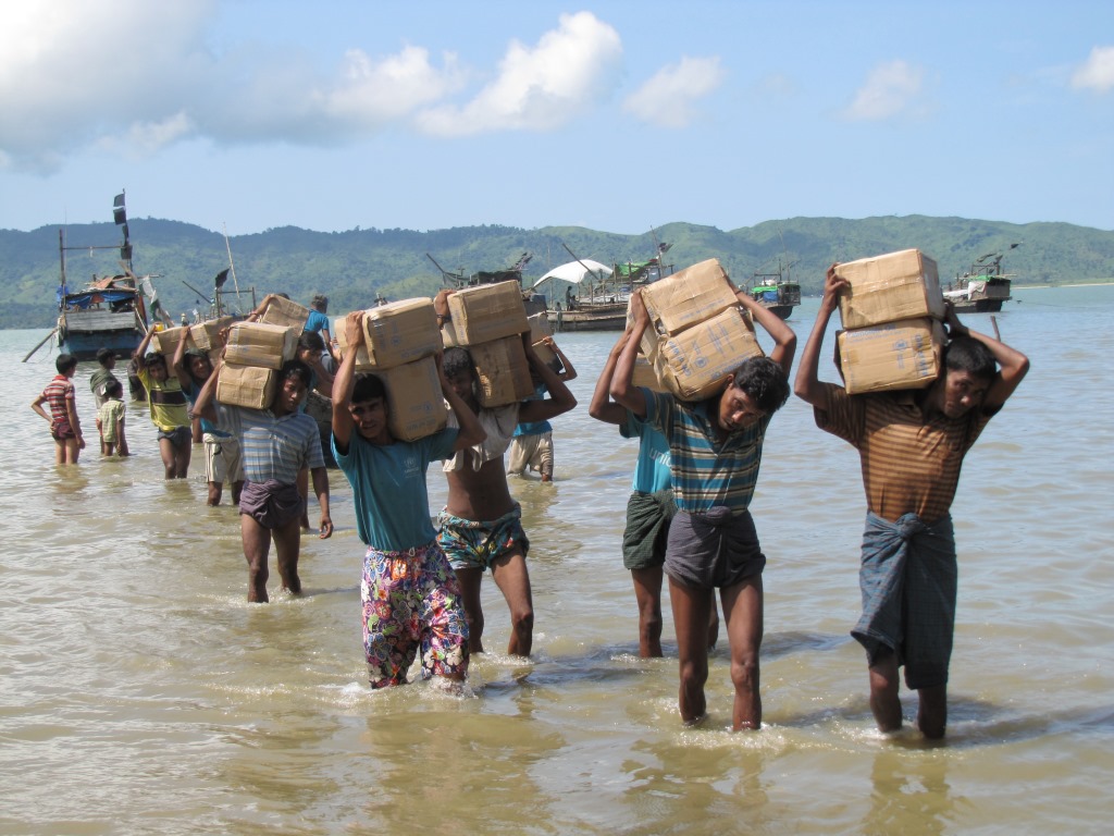 Men transport goods in cardboard boxes over their shoulder to an IDP camp for Rohingyas near Sittwe, Myanmar.