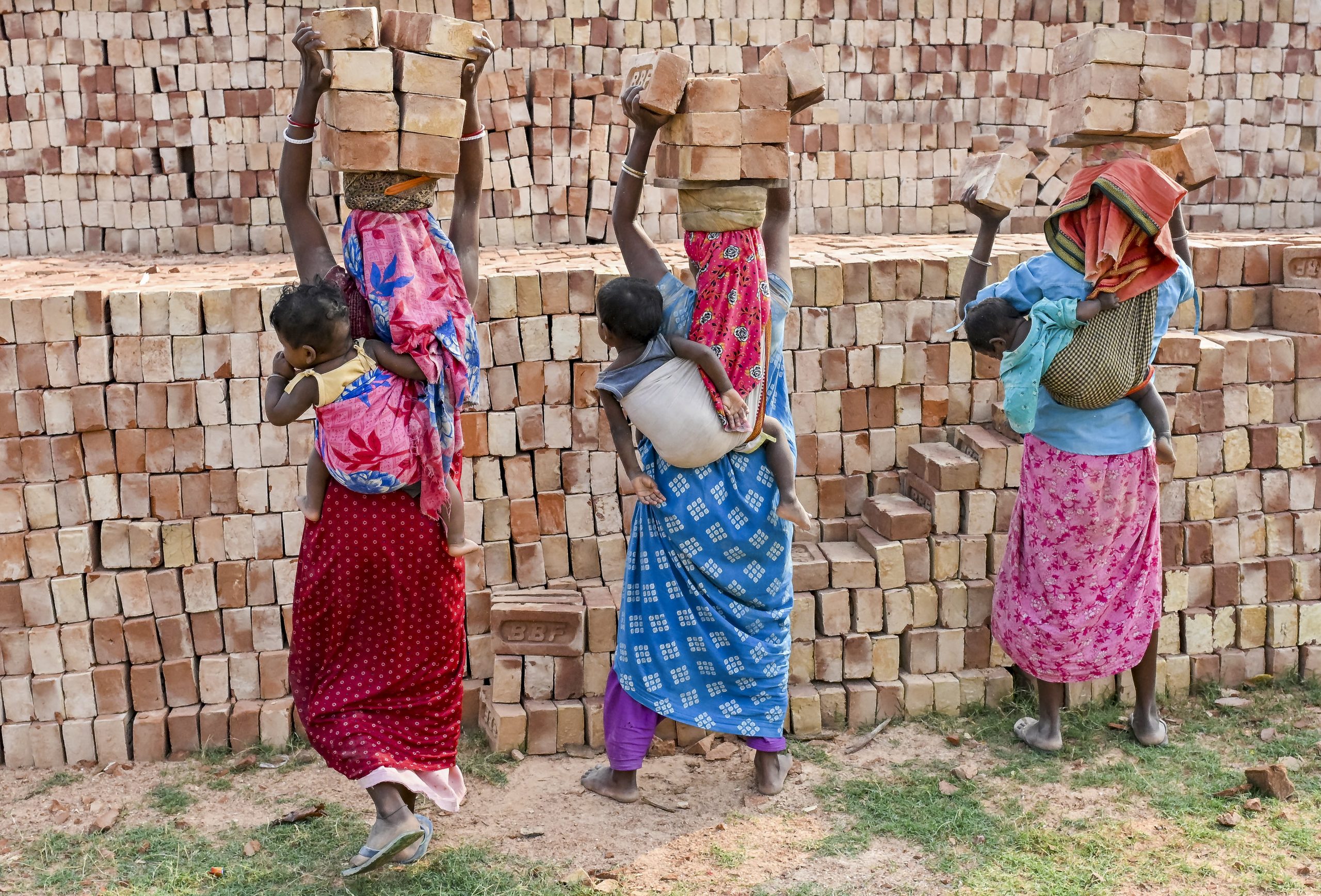 Women labourers, carrying their children, work at a brick kiln factory,
