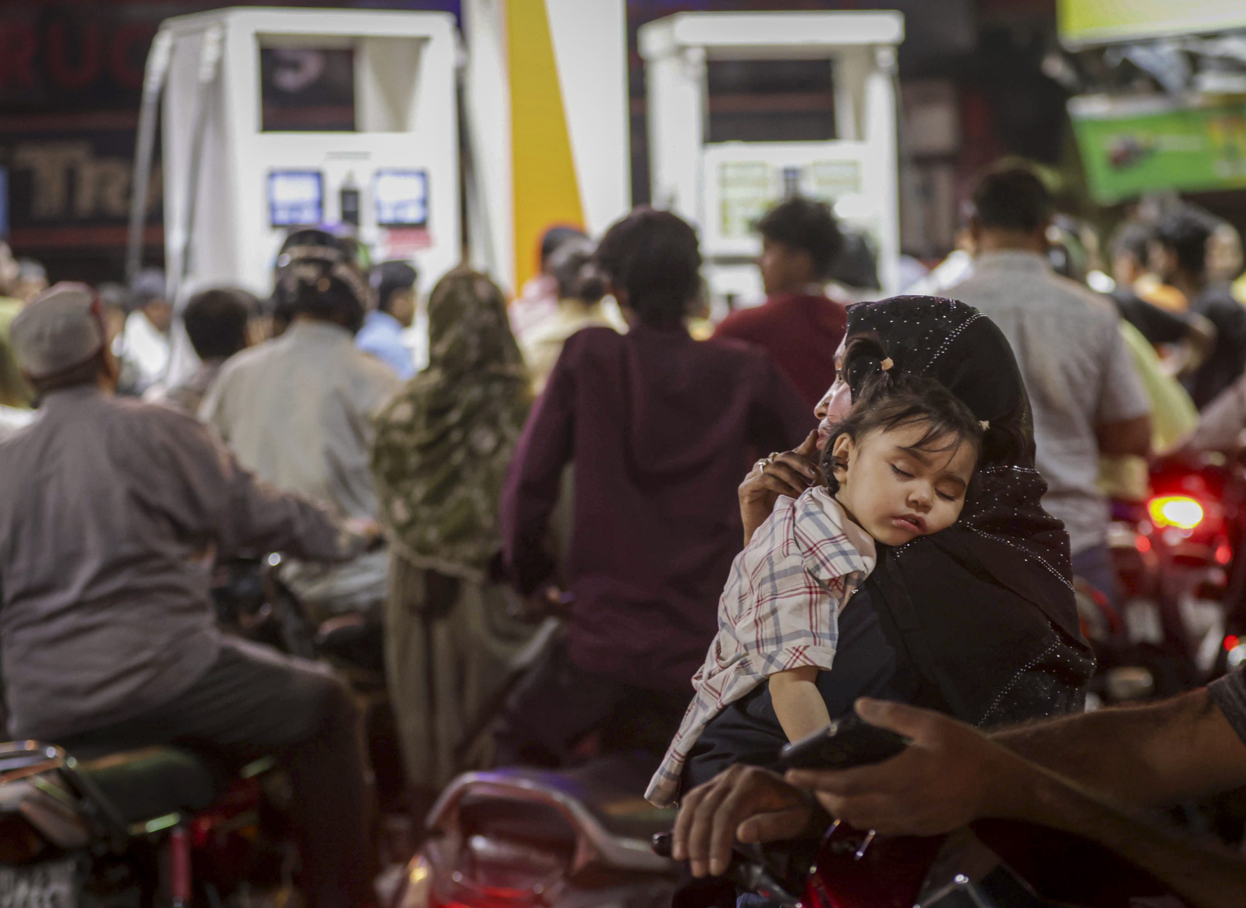 A woman with a sleeping child as her husband fill fuel in his vehicle at a petrol pump in Prayagraj, Uttar Pradesh.